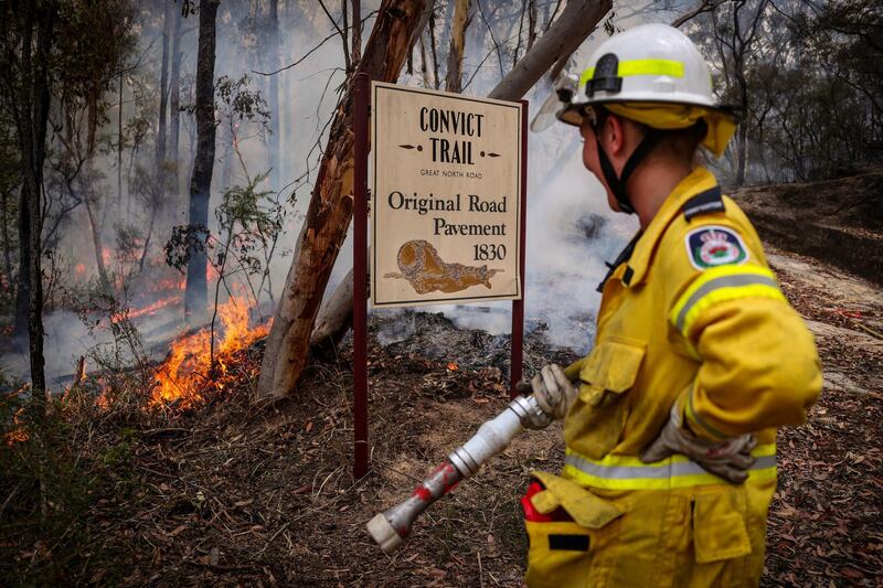 A New South Wales (NSW) Rural Fire Service volunteer watches a fire next to a sign, indicating the site of a convict-built road, during back-burning operations in bushland near the town of Kulnura, New South Wales, Australia. Bloomberg