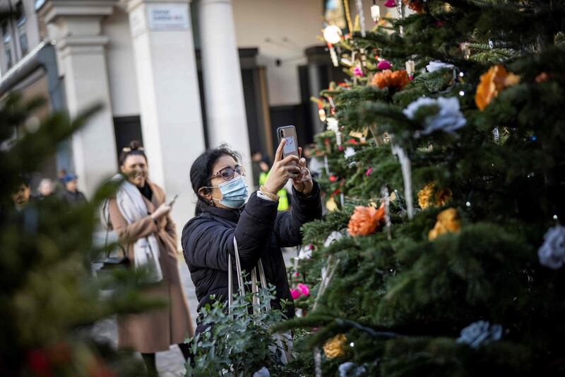 A woman wearing a protective face covering takes a picture of a Christmas tree in Covent Garden in central London. AFP