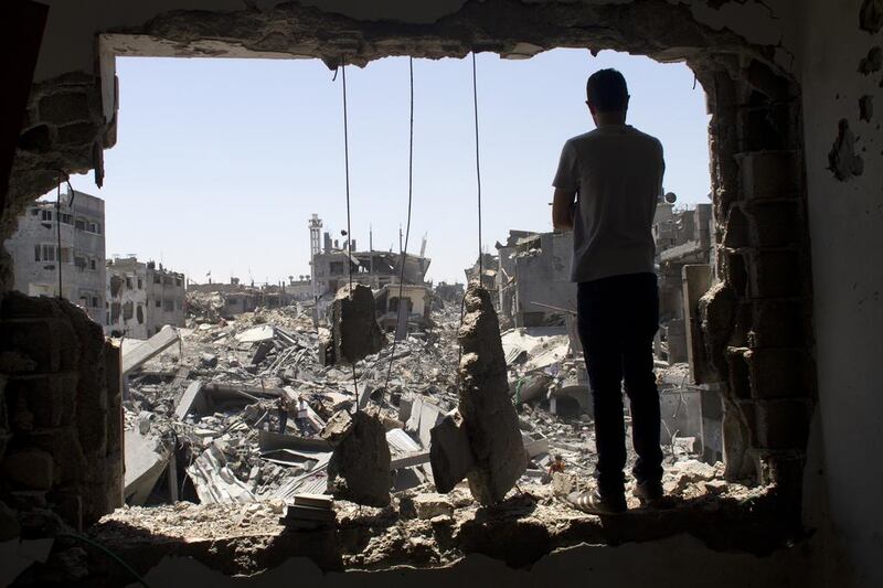 A Palestinian stands in a damaged window against the massive destruction of a homes reduced to rubble.