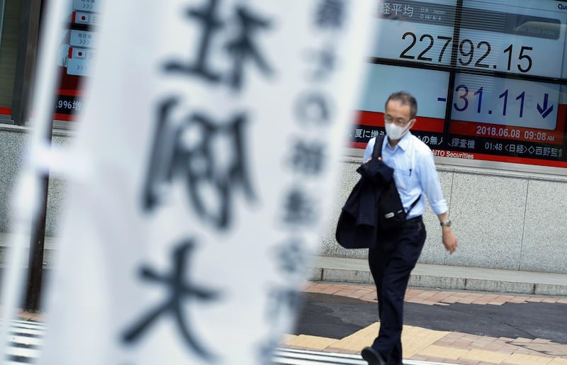 A man walks past an electronic stock board showing Japan's Nikkei 225 index at a securities firm near a banner of a festival in Tokyo Friday, June 8, 2018. Asian shares were moderately lower Friday, as investors awaited the Group of Seven leaders' meeting, continuing into the weekend, and for European Central Bank and Federal Reserve meetings next week.(AP Photo/Eugene Hoshiko)