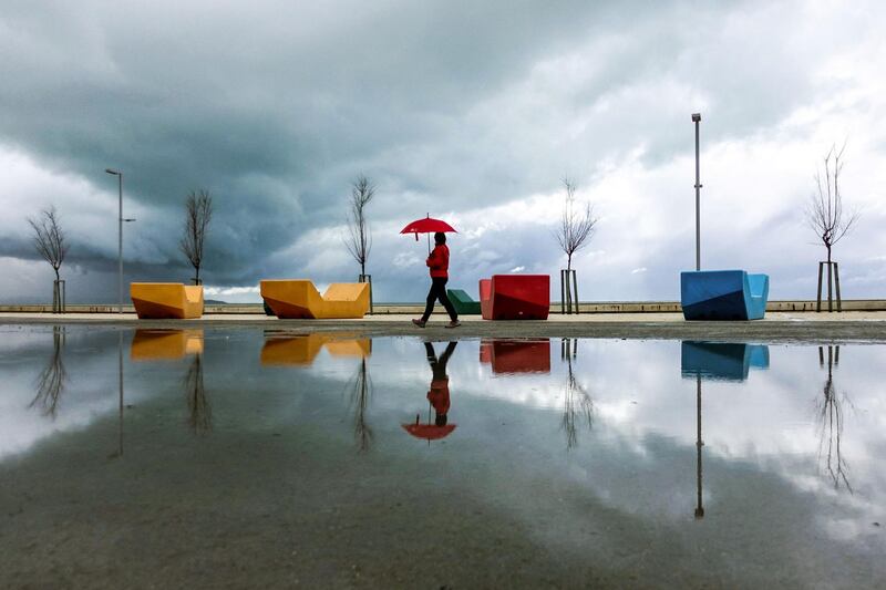 A woman with an umbrella walks on the promenade in the city of Durres, Albania, as a storm brews in the background. AFP