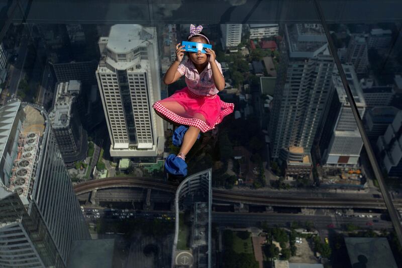 A girl watches a partial solar eclipse on the Mahanakhon Skywalk Glass Tray at the King Power Mahanakhon building in Bangkok, Thailand. Reuters