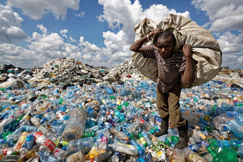 A man walks on a mountain of plastic bottles as he carries a sack of them to be sold for recycling at the dump in the Dandora slum of Nairobi, Kenya. AP Photo