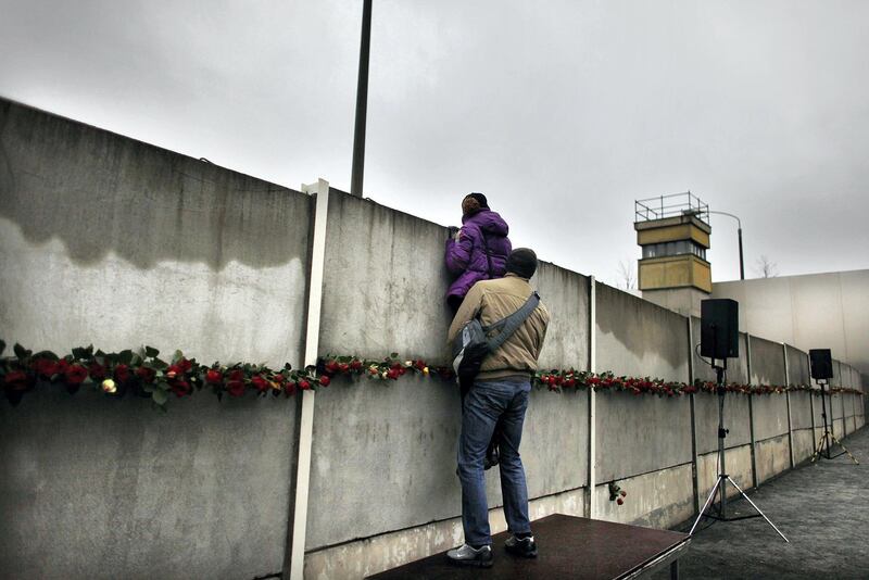 BERLIN - NOVEMBER 09:  A couple attempts to peek through cracks and among roses left by visitors in a still-existing section of the Berlin Wall into the so-called 'death strip,' where East German border guards had the order to shoot anyone attempting to flee into West Berlin, at the Bernauer Strasse memorial on the 20th anniversary of the fall of the Wall on November 9, 2009 in Berlin, Germany. The city of Berlin is celebrating the 20th anniversary of the fall of the Wall, which led to the end of communist rule in East Germany and later on the reunification of East and West Germany, with a spectacular event at the Brandenburg Gate and the participation of international leaders.  (Photo by Carsten Koall/Getty Images)