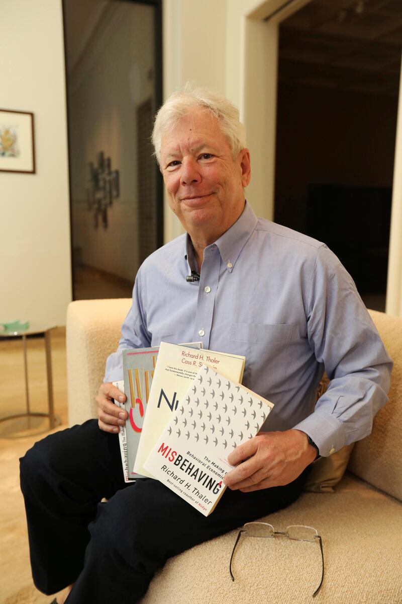 In this photo provided by the University of Chicago, Richard Thaler poses for a photo with his books at his home in Chicago after winning the Nobel prize in economics, Monday, Oct. 9, 2017. The prize was awarded to Thaler of the University of Chicago for research showing how people's choices on economic matters, whether on savings or game shows like "Deal or No Deal", are not always rational. (Anne Ryan/University of Chicago via AP)