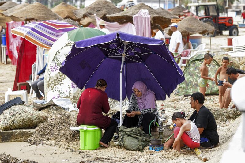 People sit in the shade of an umbrella at a beach off La Goulette (Halq al-Wadi).