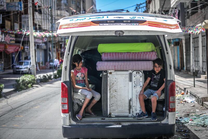 TOPSHOT - Palestinian children sit in the back of a van loaded with salvaged belongings from their home at the Al-Jawhara Tower in Gaza City, on May 17, 2021, which was heavily damaged by  Israeli airstrikes. / AFP / ANAS BABA
