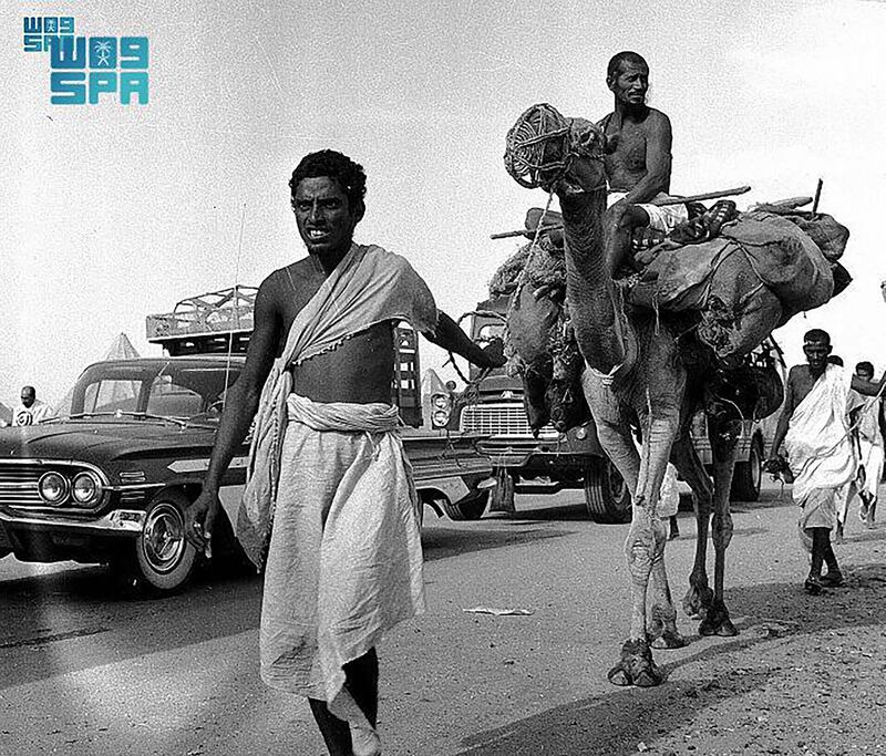 Pilgrims drive cars alongside others riding camels toward Makkah during Hajj.