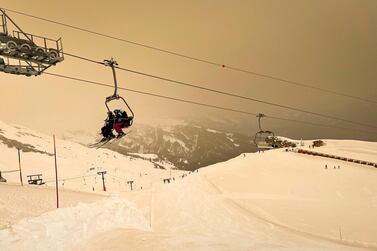 Skiers wearing protective face masks sit on a chairlift as Sahara sand colours the snow and the sky in orange and creates a special light atmosphere. AP