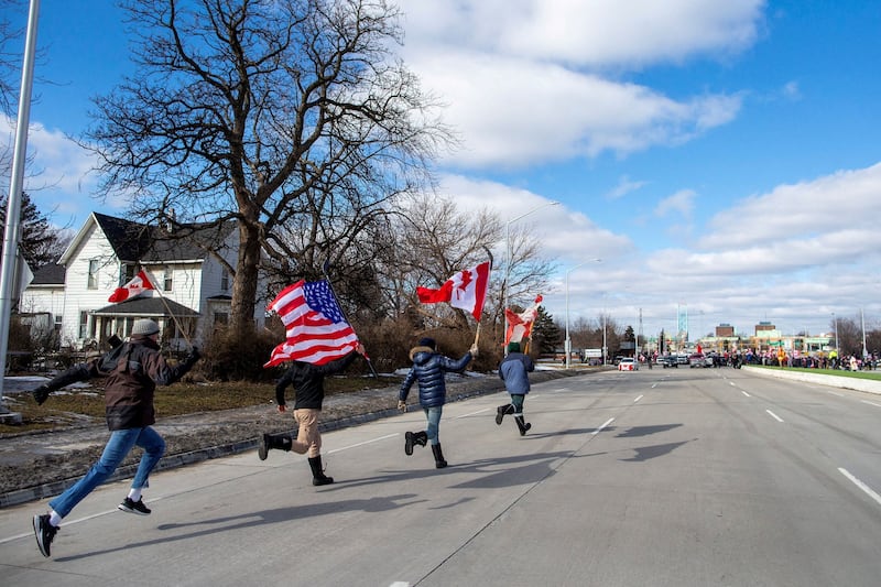 Young adults run with flags towards the protest, as truckers and supporters are moved back by the police as they continue to rally against Covid-19 vaccine mandates in Windsor, Ontario, Canada. Reuters