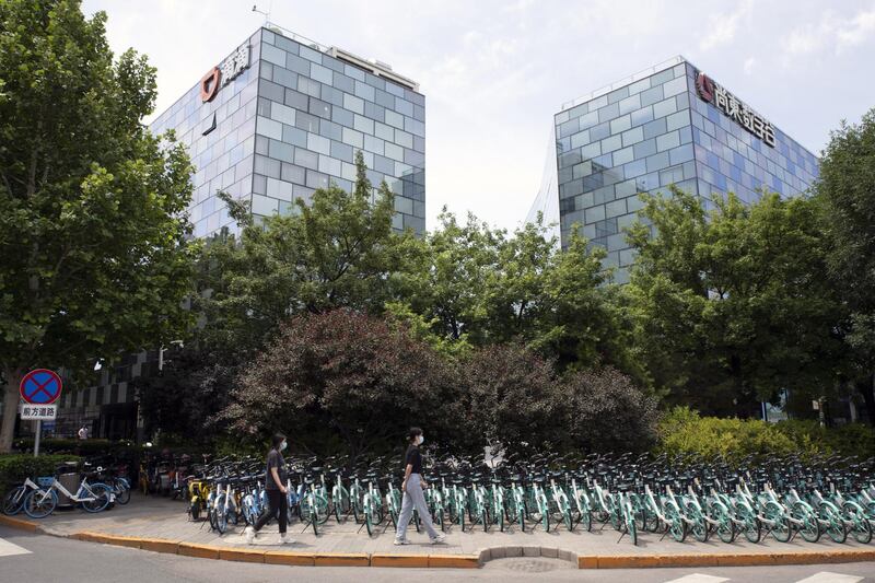 Pedestrians walk past bicycles operated by Didi's bike-sharing unit Qingju outside Didi's headquarters, left, in Beijing, China, on Friday, June 11, 2021. Chinese ride-hailing company Didi revealed a $1.6 billion net loss for 2020 as it moves ahead with plans for a U.S. initial public offering. Photographer: Gilles Sabrie/Bloomberg
