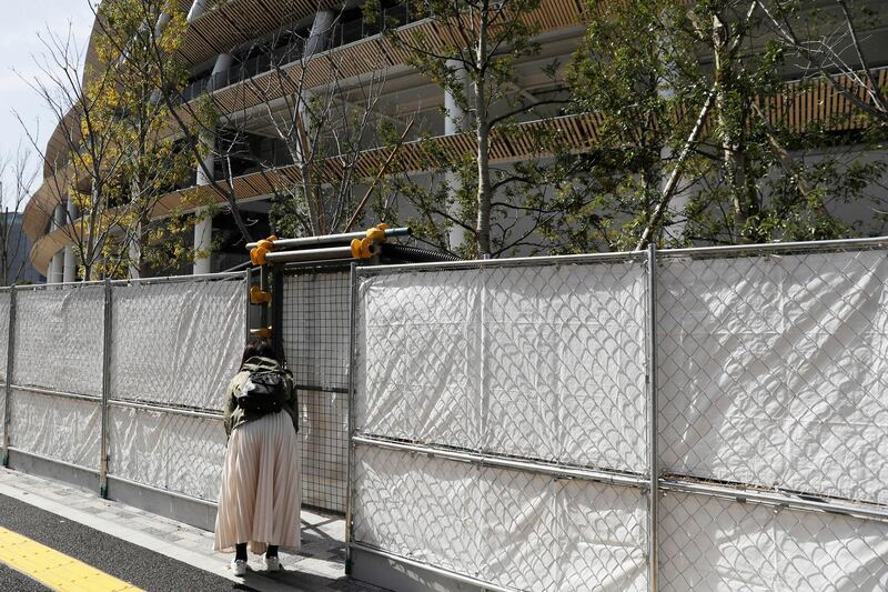 A woman peeks through a fence surrounding the Olympic Stadium in Tokyo on Saturday. AP