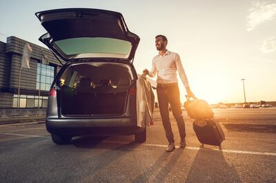 Happy businessman going on a business travel but first he has to pack his stuff into the car.