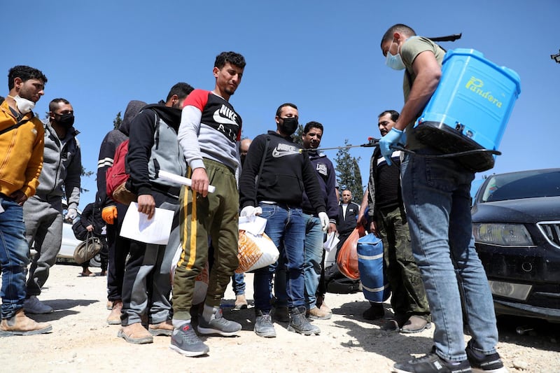 An employee of the Palestinian health ministry sprays disinfectant on workers crossing the checkpoint of Tarqumiya, near the West Bank town of Hebron. EPA