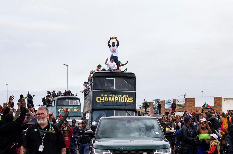 People cheer as South African Rugby captain Siya Kolisi (C) holds up the Web Ellis Trophy while the South African Rugby World Cup winner team parades on an open top bus through the streets of the city of Zwide . AFP