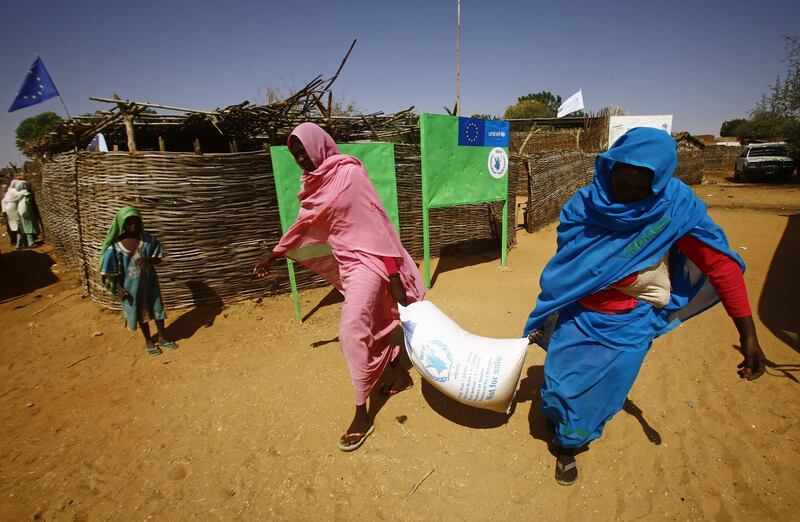 (FILES) In this file photo taken on February 8, 2017, Sudanese women carry a bag of aid at the al-Riyadh camp for internally displaced persons (IDP) in Geneina, the capital of the state of West Darfur. Ongoing clashes in Sudan's restive Darfur have killed at least 48 people in two days, state media said, just over two weeks after a long-running peacekeeping mission ended operations. The violence has pitted the Massalit tribe against Arab nomads in El Geneina, the capital of West Darfur state, but later morphed into broader fighting involving armed militias in the area. / AFP / ASHRAF SHAZLY
