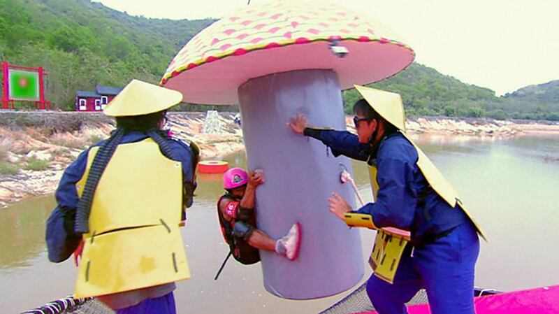 A Takeshi's Castle contestant hangs onto a giant inflatable mushroom as two of the show's characters try to dislodge him. Takeshi's Castle