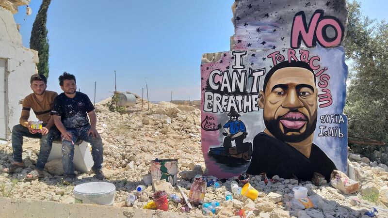Aziz Asmar, right, and Anis Hamdoun, sitting in front of their mural of George Floyd in Idlib, Syria. 'When we draw on the walls of destroyed buildings, we are telling the world that underneath these buildings there are people who have died or who have left their homes... there was injustice here, just like there's injustice in America'. Aziz Asmar