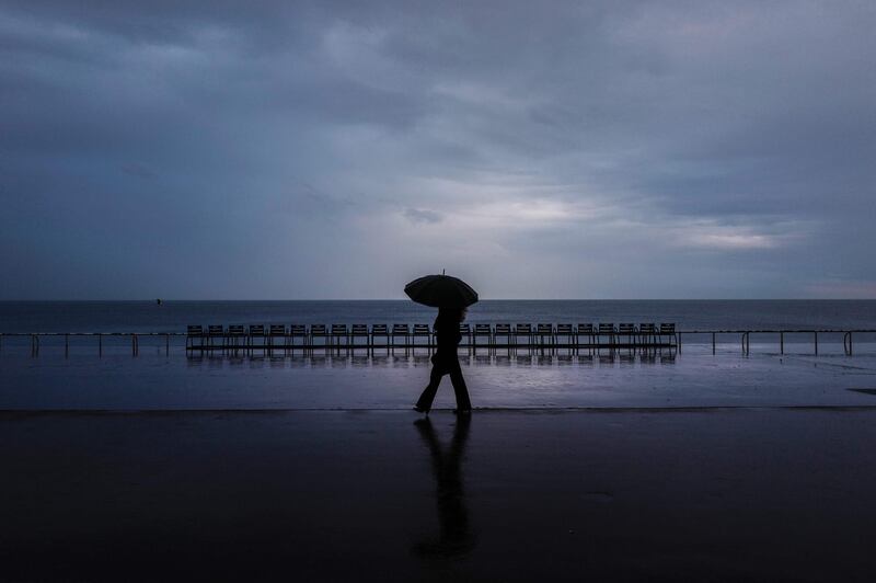A woman walks with an umbrella on a shingle beach along the "Promenade des anglais" on the French riviera city of Nice. AFP