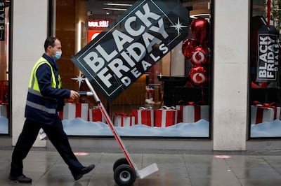 A delivery man walks in the rain past Black Friday offers in a shop in central London on November 20, 2020, as life under a second lockdown continues in England.  The current lockdown in England has shuttered restaurants, gyms and non-essential shops and services until December 2, with hopes business could resume in time for Christmas. / AFP / Tolga Akmen
