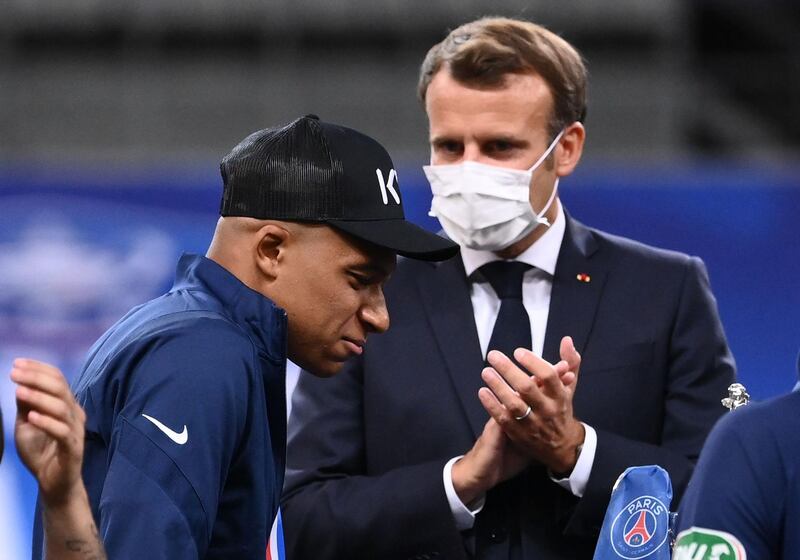 French President Emmanuel  Macron applauds as Paris Saint-Germain's Kylian Mbappe walks  with crutches onto a platform for the trophy ceremony. AFP