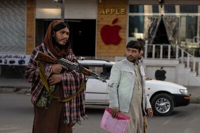 An Afghan man passes a Taliban fighter standing guard at a check point, in Kabul. AP