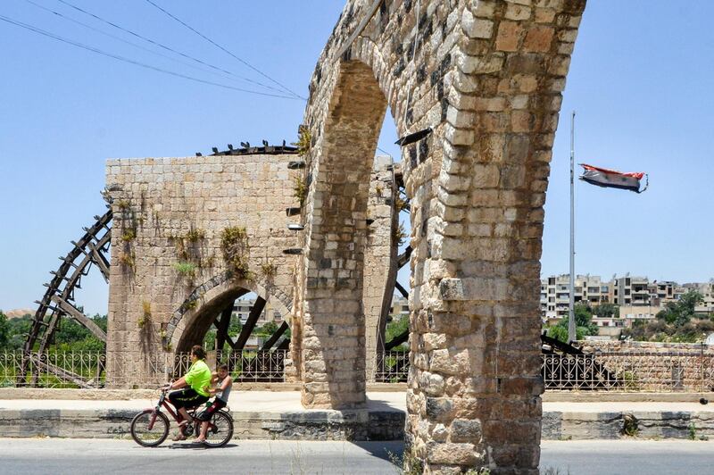 Two boys ride a bicycle along a road crossing beneath an aqueduct reaching to the Dawalek Noria (water wheel) along the Orontes (Assi) river in the city of Hama in west-central Syria. Used for centuries to bring water to gardens and buildings on the shores of the Orontes river, the water wheels or norias of Hama are believed to be unique worldwide, according to Unesco. AFP
