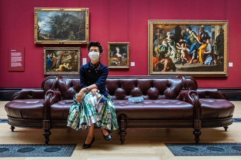 A woman wearing a face mask sits on a bench at the 'Love, Desire, Death' exhibition during preparations for opening at the National Gallery London on Saturday, July 4. Pubs, restaurants, places of worship, hairdressers and other businesses are reopening their doors across the UK after more than three months of lockdown due to the coronavirus pandemic. EPA