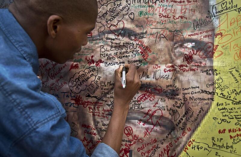 A woman writes a message on a poster of Nelson Mandela outside his old house in Soweto, South Africa. Tributes to Mandela flooded in from across the world after his death was announced on Thursday. Ben Curtis / AP Photo

