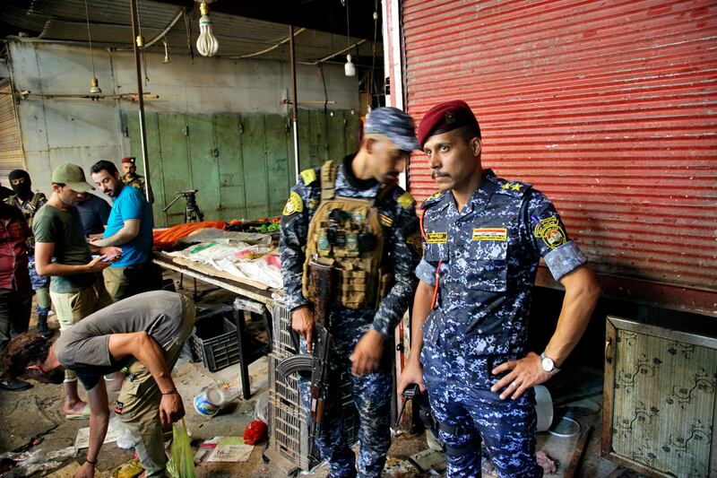 People and members of the security forces gather at the site of a bombing in Wahailat market in Sadr City, Iraq.