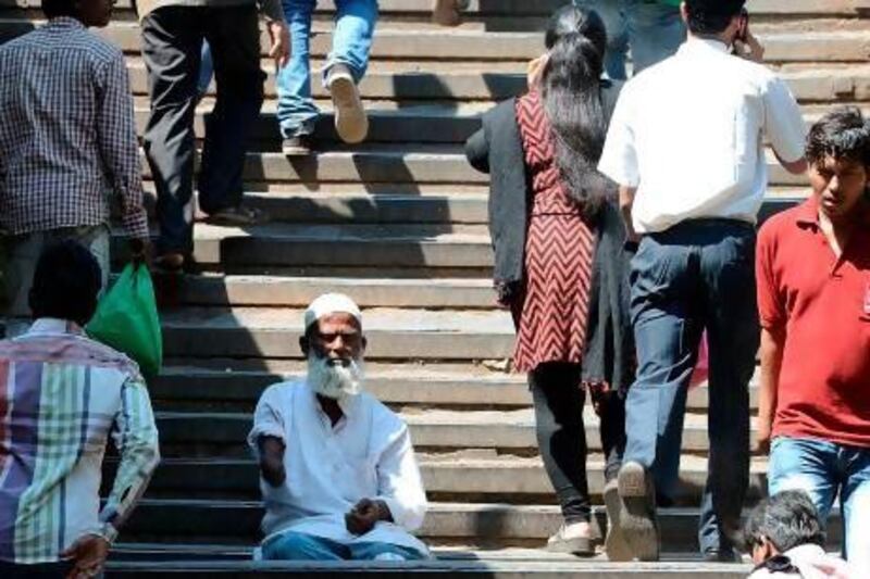 Indian pedestrians walk past a beggar sitting on steps leading to a railway station in Mumbai.