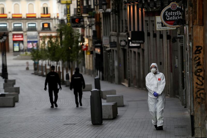 A medical worker in a protective suit walks past police officers patrolling a deserted street during the coronavirus disease (COVID-19) outbreak in Madrid, Spain March 22, 2020. REUTERS/Susana Vera