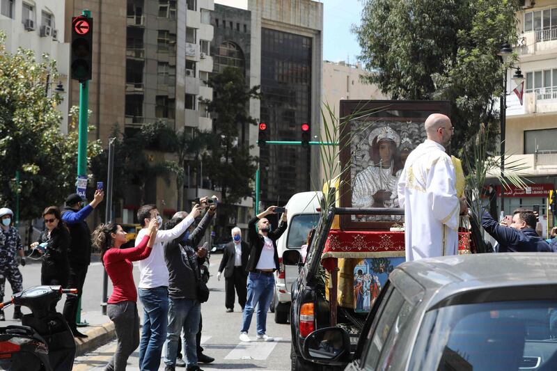 Lebanese people, some wearing protective masks amid the COVID-10 pandemic, take pictures of a car procession celebrating Palm sunday for Orthodox Christians, in the Ashrafiyeh negihborhood of the capital Beirut.  AFP
