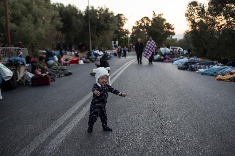 A boy tries to stand as migrants sleep on the road near the Moria refugee camp on the northeastern island of Lesbos, Greece, Thursday, Sept. 10, 2020. A second fire in Greece's notoriously overcrowded Moria refugee camp destroyed nearly everything that had been spared in the original blaze, Greece's migration ministry said Thursday, leaving thousands more people in need of emergency housing. (AP Photo/Petros Giannakouris)