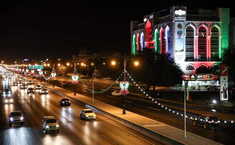 Vehicles drive along a main road past a building of the Oman Arab Bank, lit up with the national colours on the occasion of the Omani national day AFP