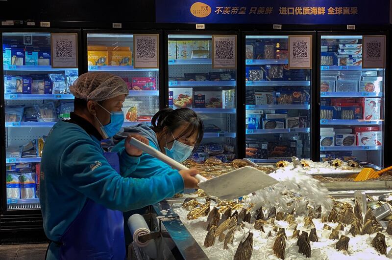 Workers wearing face masks pour ice on the clams at a section selling imported seafoods at a supermarket in Beijing. AP Photo