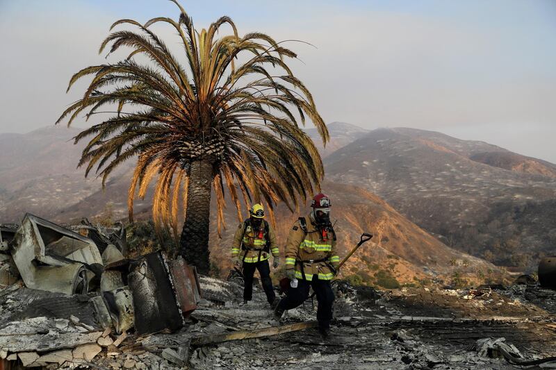 Firefighters Jason Toole, right, and Brent McGill walk among the ashes of a wildfire-ravaged home in Malibu. AP Photo