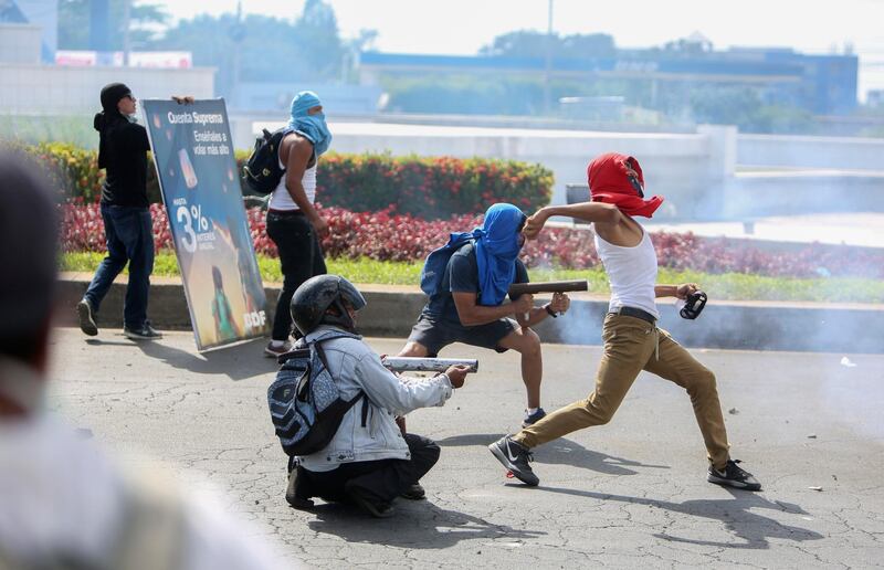 Masked protesters fire homemade mortars at riot police as another protester throws a rock during a third day of violent clashes in Managua, Nicaragua. Alfredo Zuniga / AP Photo