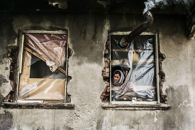 A Syrian refugee woman looks out from a window with no glass, in a house in the Kucukpazar area of Istanbul. Gurcan Ozturk / AFP