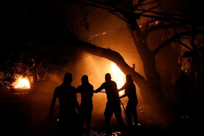 People try to extinguish a burning house during a wildfire in the Nea Kifisia suburb north of Athens.