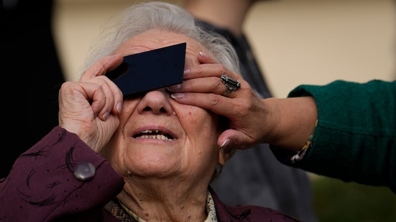 An elderly woman looks through a welding filter during a partial solar eclipse in Bucharest, Romania. AP