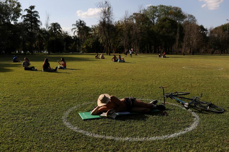 A man reads as he lies in a field where circles were painted to help visitors maintain social distancing at Ibirapuera Park after it was reopened as the city eases the restrictions imposed to control the spread of the coronavirus disease (COVID-19), in Sao Paulo, Brazil. REUTERS