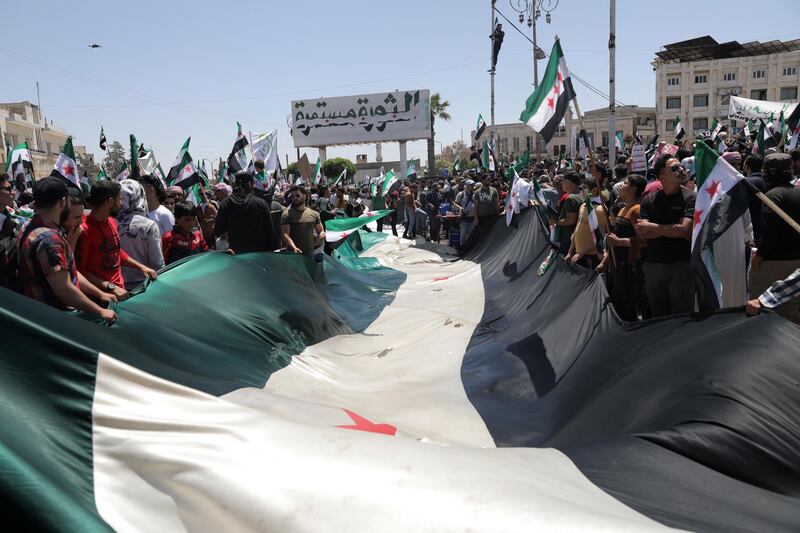 Syrian people hold placards and the Syrian opposition factions' flags as they gather under a banner reading in Arabic 'revolution continues' during a protest against the presidential elections, in Idlib. EPA