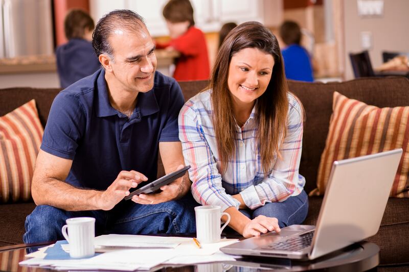 Latin descent man and woman work together to pay their monthly bills.  They are calculating expenses versus budget income on their laptop.  Many invoices on living room table.  Children in background.  Mid-adult age couple.  Middle-class people.  Great imagery for election season:  home finances, recession, budget, bills, mortgage issues, debt, taxes, e-commerce, online banking.