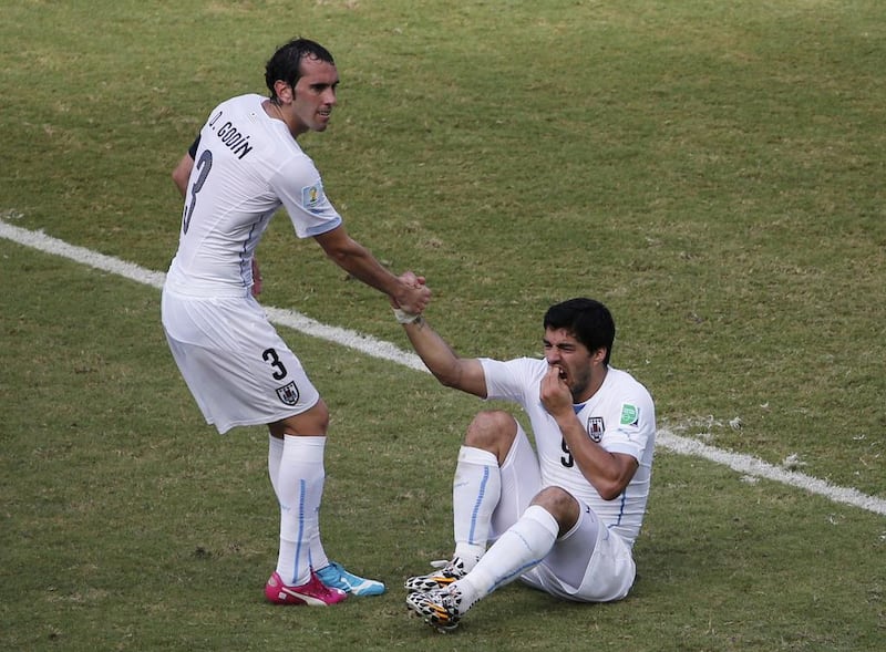 Uruguay's Luis Suarez, right, holds his teeth while sitting on the ground as teammate Diego Godin helps him up after he clashes with Giorgio Cheillini, unseen, during their match on Tuesday at the 2014 World Cup. Carlos Barria / Reuters 