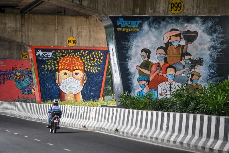 A motorist drives past coronavirus-themed murals  painted on pillars of a flyover in Noida, India. AFP