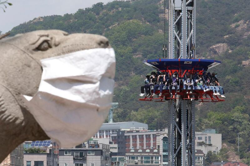 A masked statue reminds people to take precautions against coronavirus as riders on Gyro Drop enjoy Children's Day at Children's Grand Park in Seoul, South Korea. AP Photo