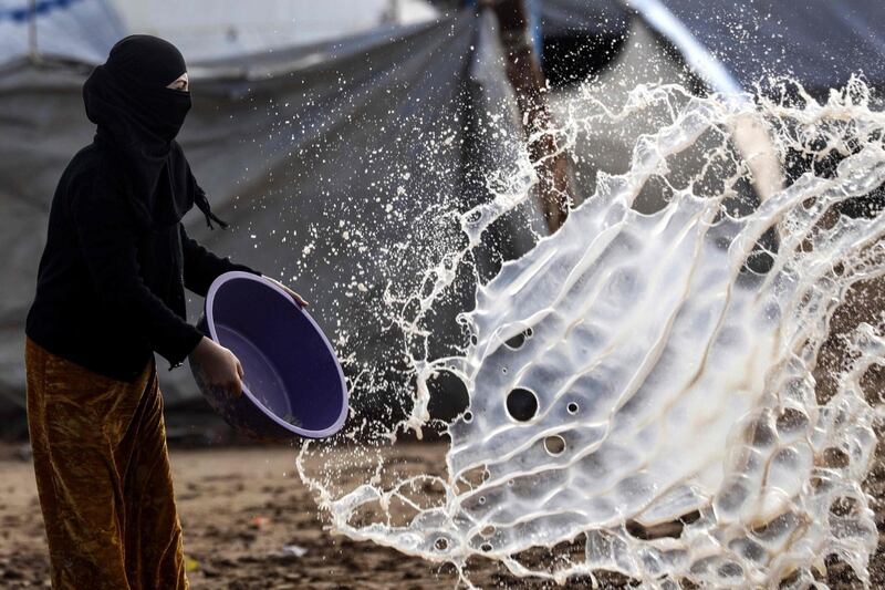 A woman empties a basin full of water at Abu Al-Khashab camp in Deir Ezzor. AFP