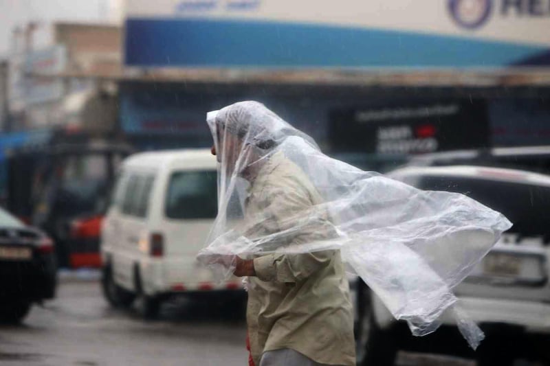 A man covers his head and shoulders with a plastic sheet as he walks through the streets of Kuwait City. AFP