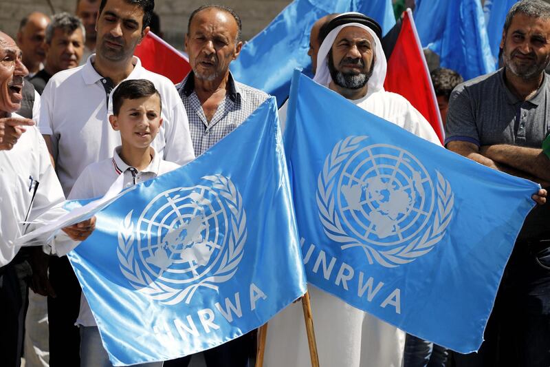 Palestinians hold placards alongside UN and the Palestinian flags in Hebron during a protest against the US cutting of aid. EPA